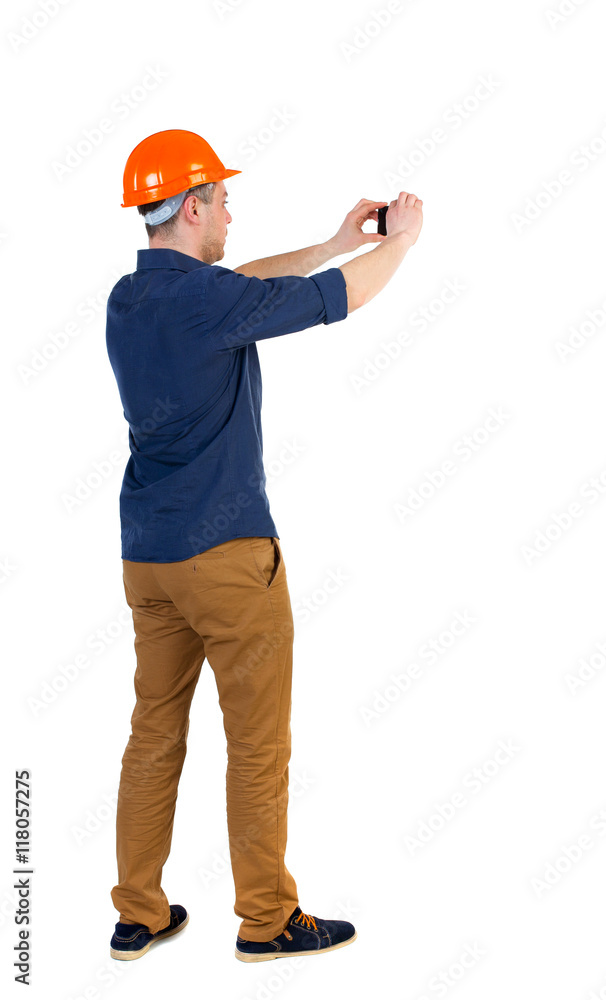 Backview of an engineer in construction helmet stands and using photo camera. Standing young guy. Rear view people collection. backside view of person. Isolated over white background. a man in a Backview of an engineer in construction helmet stands and using photo camera. Standing young guy. Rear view people collection. backside view of person. Isolated over white background. a man in a