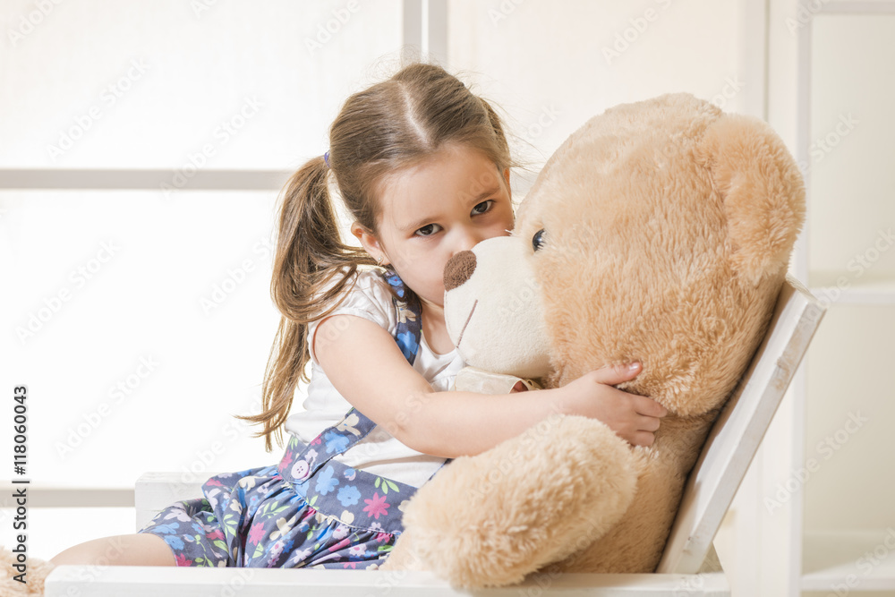 Portrait of expressive little girl hugging and kissing huge plush bear indoor shot on white room. Little girl playing with teddy bear Stock Adobe Stock