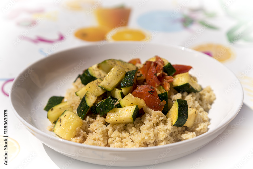 Close up on small plate full of cooked couscous with zucchini and tomato slices Close up on small plate full of cooked couscous with zucchini and tomato slices