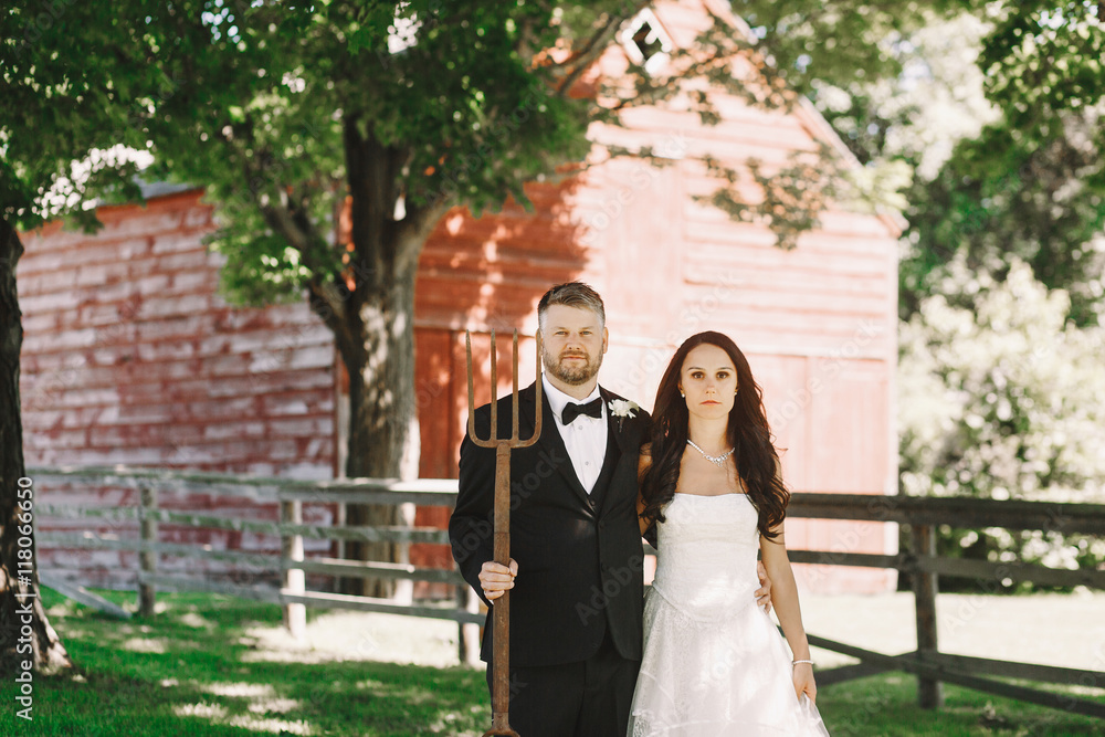 Newlyweds look serious while posing with pitchfor on the backyar Newlyweds look serious while posing with pitchfor on the backyar