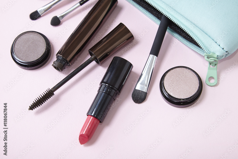 A make up bag with beauty products spilling out on to a pastel pink background A make up bag with beauty products spilling out on to a pastel pink background