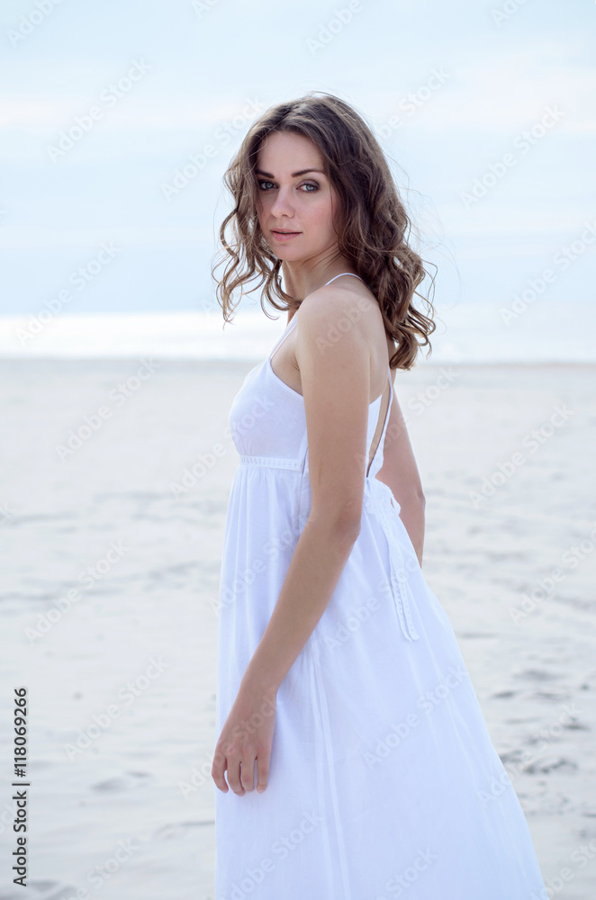 Beautiful woman in a white dress on the ocean coast. Happy girl on the beach, the wind fluttering hair. Beach vacation. Beautiful woman in a white dress on the ocean coast. Happy girl on the beach, the wind fluttering hair. Beach vacation.