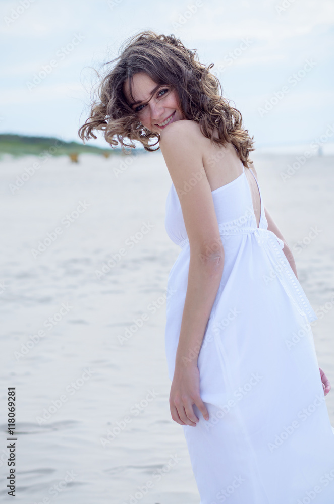 Beautiful woman in a white dress on the ocean coast. Happy girl on the beach, the wind fluttering hair. Beach vacation. Beautiful woman in a white dress on the ocean coast. Happy girl on the beach, the wind fluttering hair. Beach vacation.