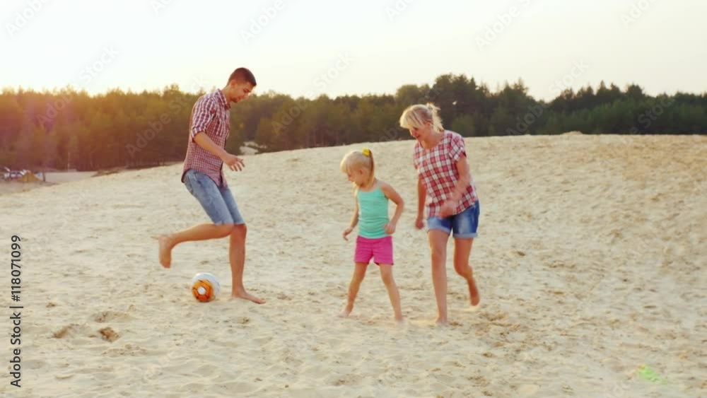 Families with a child playing football in the sand on the beach Families with a child playing football in the sand on the beach