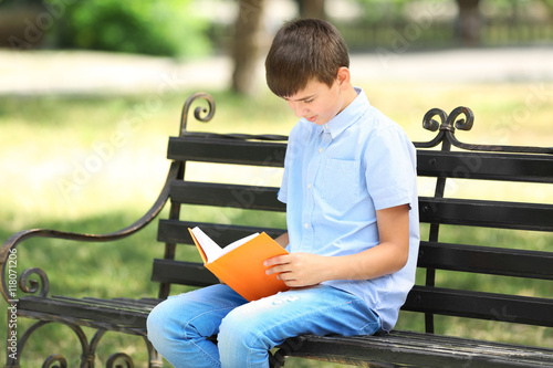 Cute boy reading book on bench