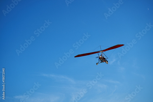 Red motor hang glider flying in the blue sky.