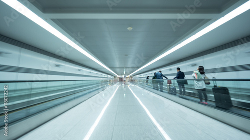 Perspective view of the airport tunnel. Light walkway equipped with flat escalators and people with luggage riding it. Faces unidentified. Seoul, South Korea