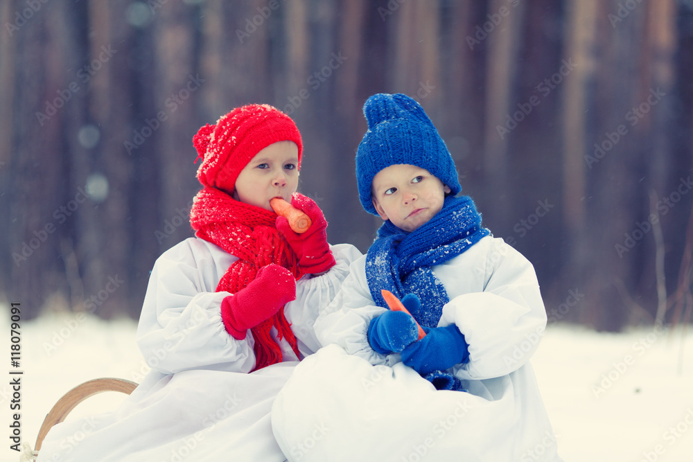 Happy brother and sister in costumes snowman walking in winter forest