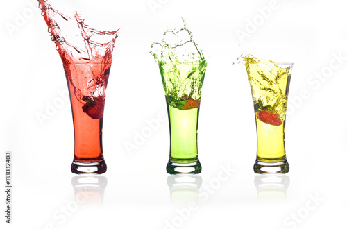 Splash of strawberry thrown into a glass. Three different colored drinks with strawberries, yellow, green and red.