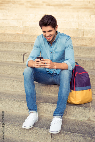 happy smiling young man sitting on the stairs with phone