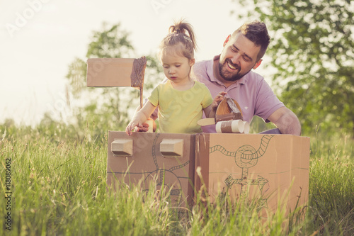 Father and toddler girl playing with paperboard ship in the yard