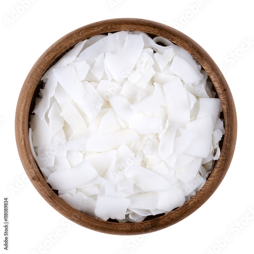 Coconut flakes in a bowl on white background, also called copra. Dried and grated flesh or meat of the coconut kernel. Edible, raw and organic food. Isolated close up macro photo from above.