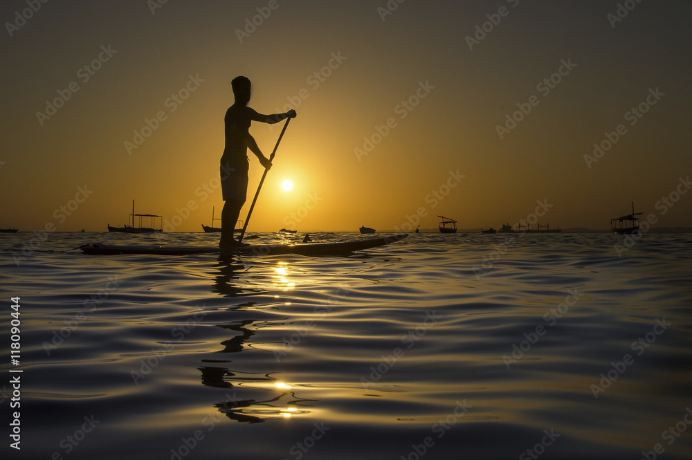 Silhouette of man paddling on paddle board at sunset.