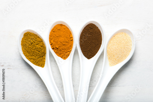 variety of spices (allspice, turmeric, garlic powder, curry) in white spoons, overhead view
