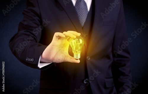 man in suit holding a glowing yellow light bulb