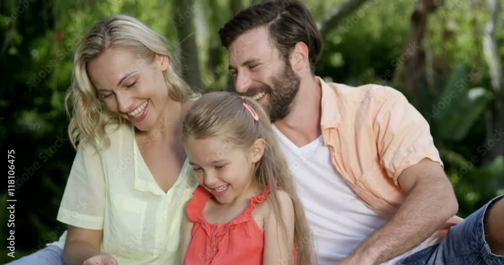 Cute family are sitting on the grass and looking a smartphone in the garden Cute family are sitting on the grass and looking a smartphone in the garden