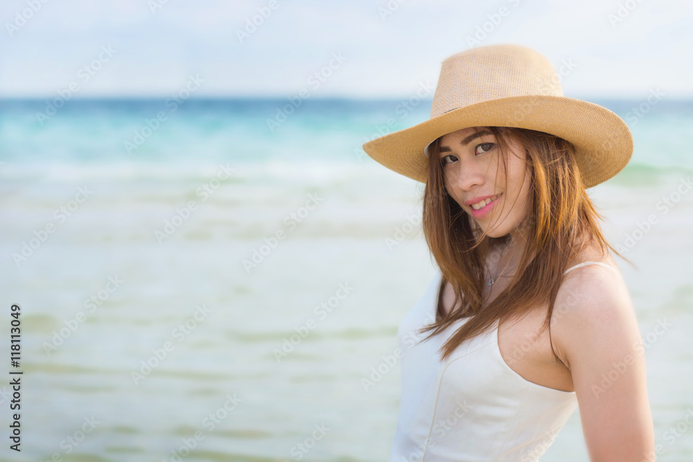 Young woman in long white dress and hat leying on white sand of tropical beach having great summer time on holidays.
