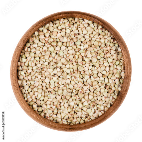 Buckwheat in a wooden bowl on white background. Small grain seeds of Fagopyrum esculentum. Edible, raw and organic food. Isolated close up macro photo.