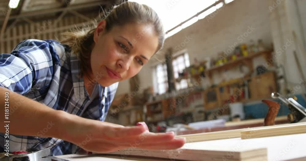 Beautiful carpenter blowing on wooden plank 
