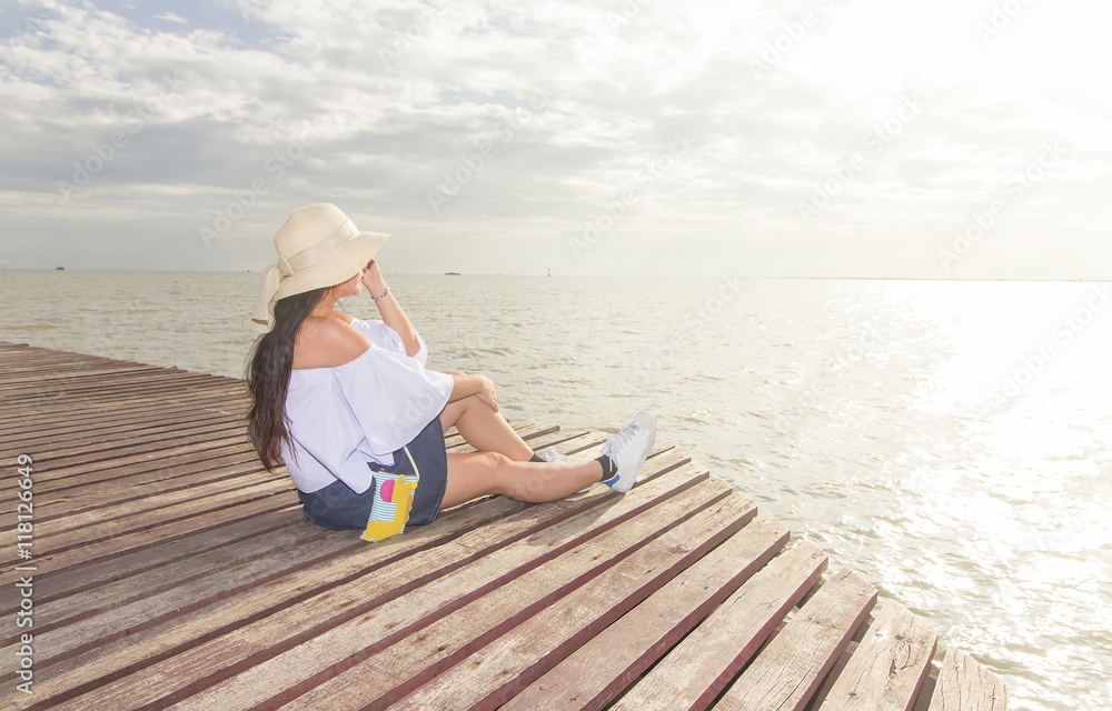 Beautiful  Asian woman sittig on wooden bridge in the sea in the morning with the sun shining.