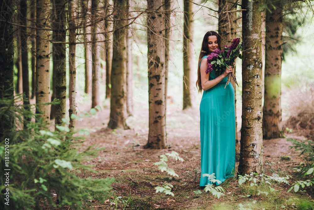 Portrait of a beautiful brunet pregnant girl in a green dress, dreamy and standing in the forest between the pines. Pregnant woman in the park. Portrait of a beautiful brunet pregnant girl in a green dress, dreamy and standing in the forest between the pines. Pregnant woman in the park.