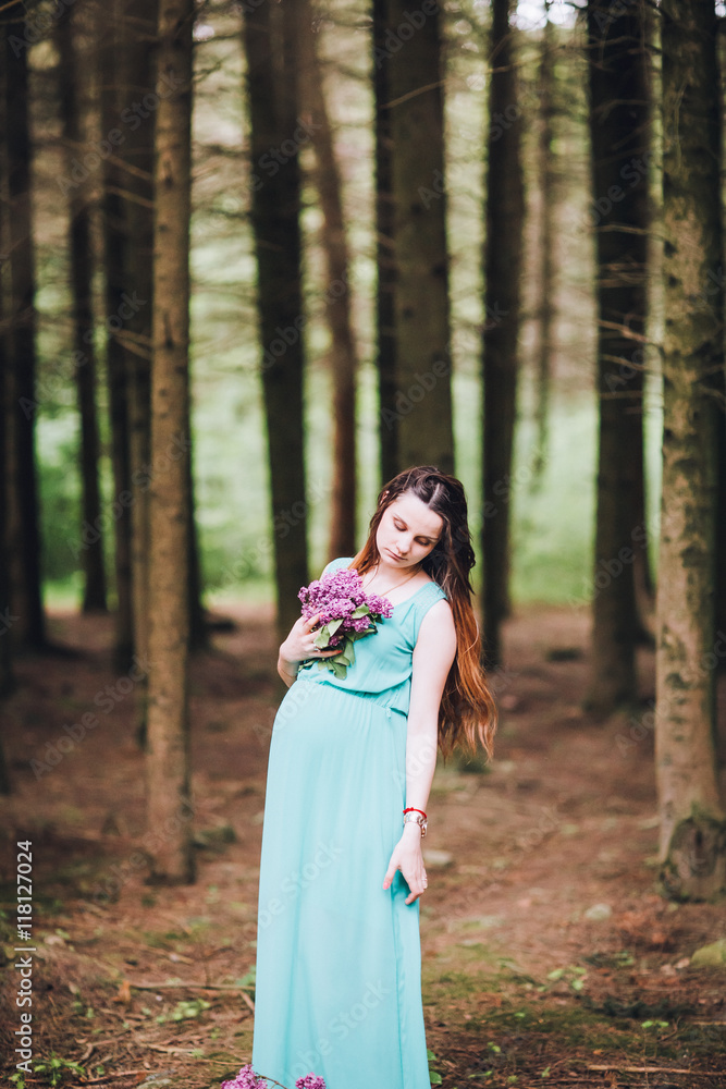 Portrait of a beautiful brunet pregnant girl in a green dress, dreamy and standing in the forest between the pines. Pregnant woman in the park. Portrait of a beautiful brunet pregnant girl in a green dress, dreamy and standing in the forest between the pines. Pregnant woman in the park.