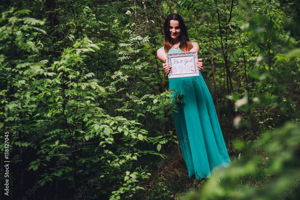 Portrait of a beautiful brunet pregnant girl in a green dress, dreamy and standing in the forest between the pines. Pregnant woman in the park. Portrait of a beautiful brunet pregnant girl in a green dress, dreamy and standing in the forest between the pines. Pregnant woman in the park.