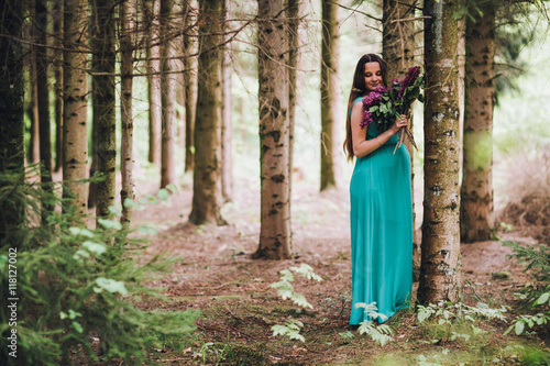 Portrait of a beautiful brunet  pregnant girl in a green dress  dreamy and standing in the forest between the pines. Pregnant woman in the park.