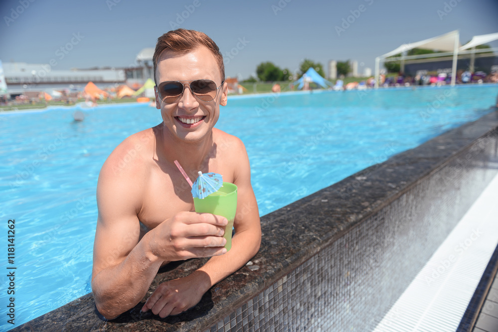 Cheerful guy drinking cocktail in pool