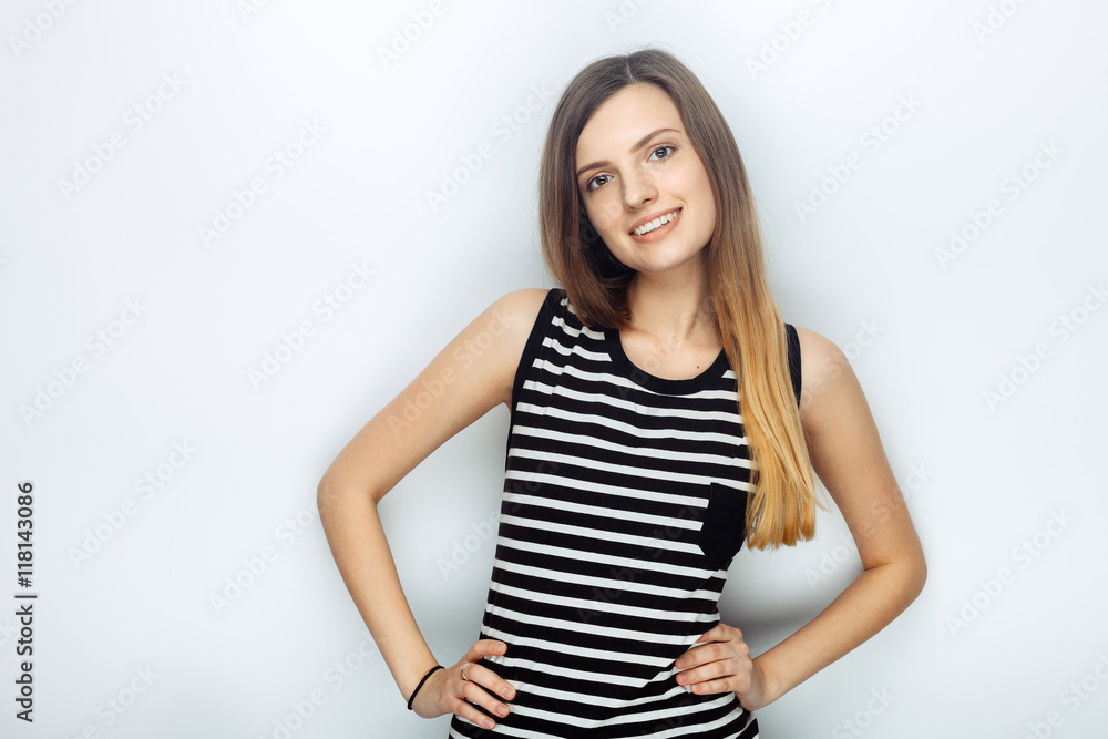 Portrait of happy young beautiful woman in striped shirt posing with hands on hips for model tests against studio background Portrait of happy young beautiful woman in striped shirt posing with hands on hips for model tests against studio background