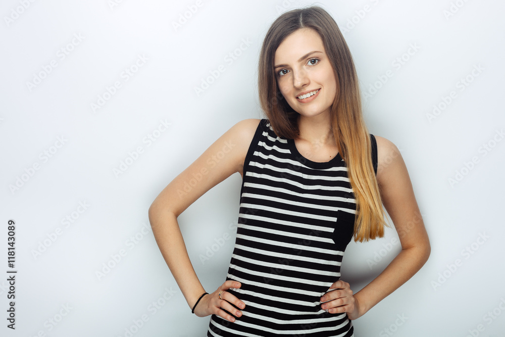 Obraz premium Portrait of happy young beautiful woman in striped shirt posing with hands on hips for model tests against studio background