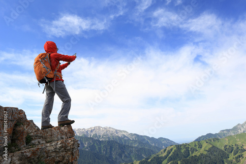 successful woman backpacker use digital tablet taking photo on mountain peak cliff