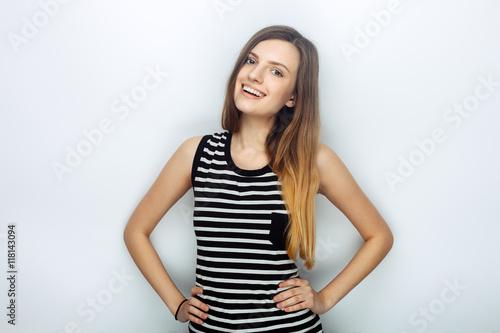 Portrait of happy young beautiful woman in striped shirt posing with hands on hips for model tests against studio background