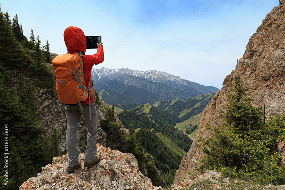 successful woman backpacker use digital tablet taking photo on mountain peak cliff