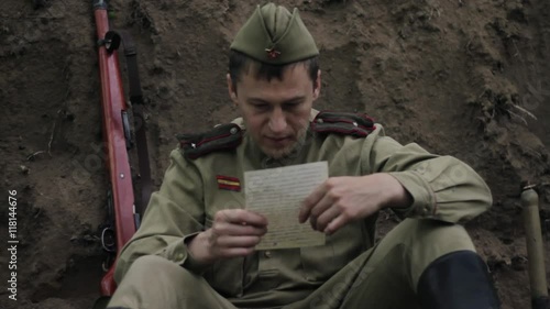 Soviet soldier sits in trench and reads a letter from home. World War II.