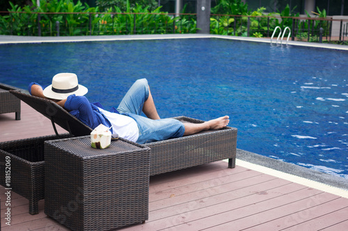man lying on deck chairs next to a swimming pool
