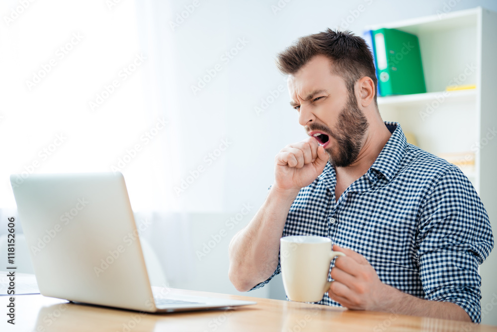 Young businessman yawning and drinking coffee to be energetic Young businessman yawning and drinking coffee to be energetic