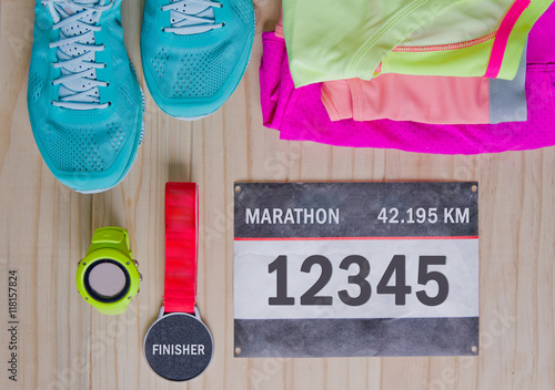 Foto Top view of outfit for runner on wooden background: bib number, finisher medal, gps watch, running shoes, shorts, shirt, and sport bra
