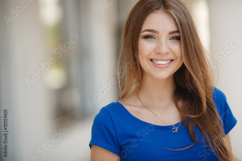 Beautiful young woman brunette with long straight hair,long black eyelashes,pretty smile,white straight teeth,wearing a blue summer dress,posing on light gray background