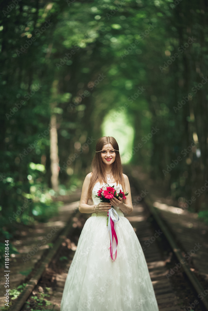 Beautiful brunette bride in elegant white dress holding bouquet posing neat trees Beautiful brunette bride in elegant white dress holding bouquet posing neat trees