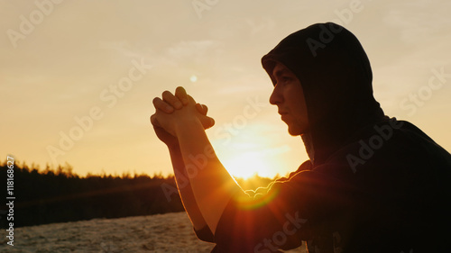 A young man in a hood dreams at sunset or praying