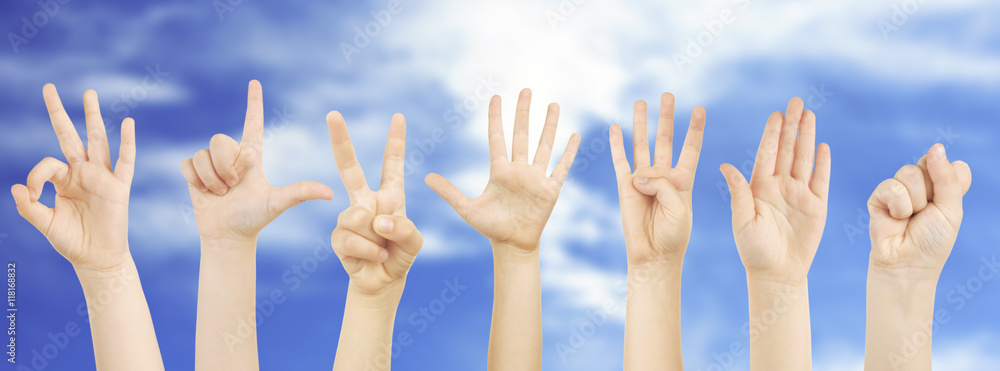 Children hands showing gestures on sky background.