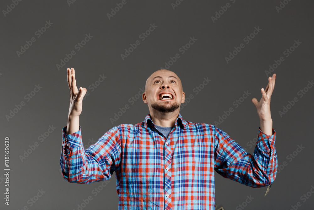 Naklejka premium Portrait of handsome middle-aged man screaming up lifting hands in plaid shirt over grey background.