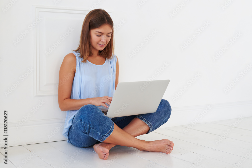 Young trendy girl is texting on her laptop while sitting on the Young trendy girl is texting on her laptop while sitting on the