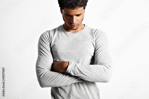 Sad or preoccupied looking thoughtful young muscular black man in light heather gray cotton longsleeve t-shirt with his arms crossed isolated on white photo