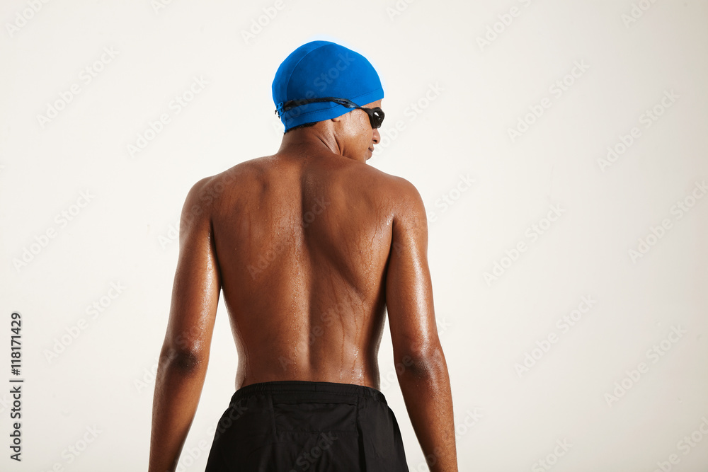 Back shot of the muscular wet back of a young strong African American swimmer in blue cap, black goggles and black shorts isolated on white Back shot of the muscular wet back of a young strong African American swimmer in blue cap, black goggles and black shorts isolated on white