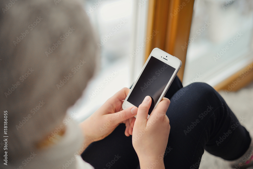 Cute girl with long hair sitting alone near window with mobile phone Cute girl with long hair sitting alone near window with mobile phone