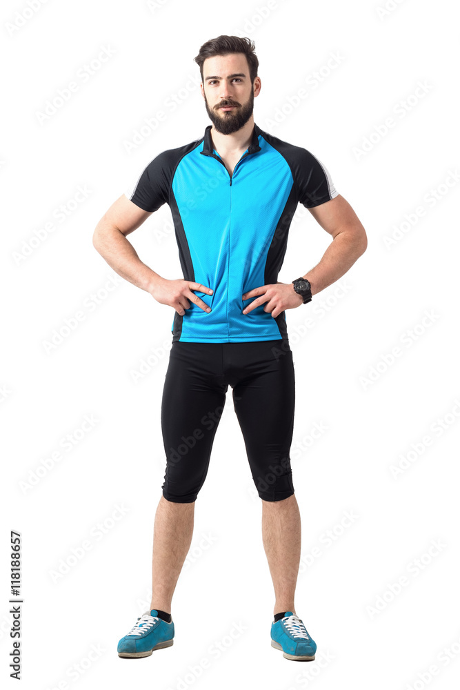 Obraz premium Fit young bearded athlete in cycling sportswear with arms on hips looking at camera. Full body length portrait isolated over white studio background.