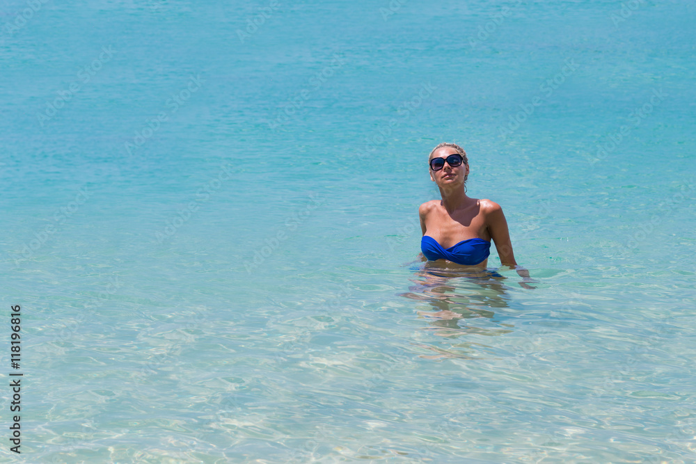 Slim blonde woman swimming in clear water on tropic beach