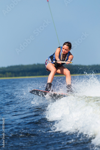 Slim brunette woman riding wakeboard on motorboat wave in lake © AnnaMoskvina